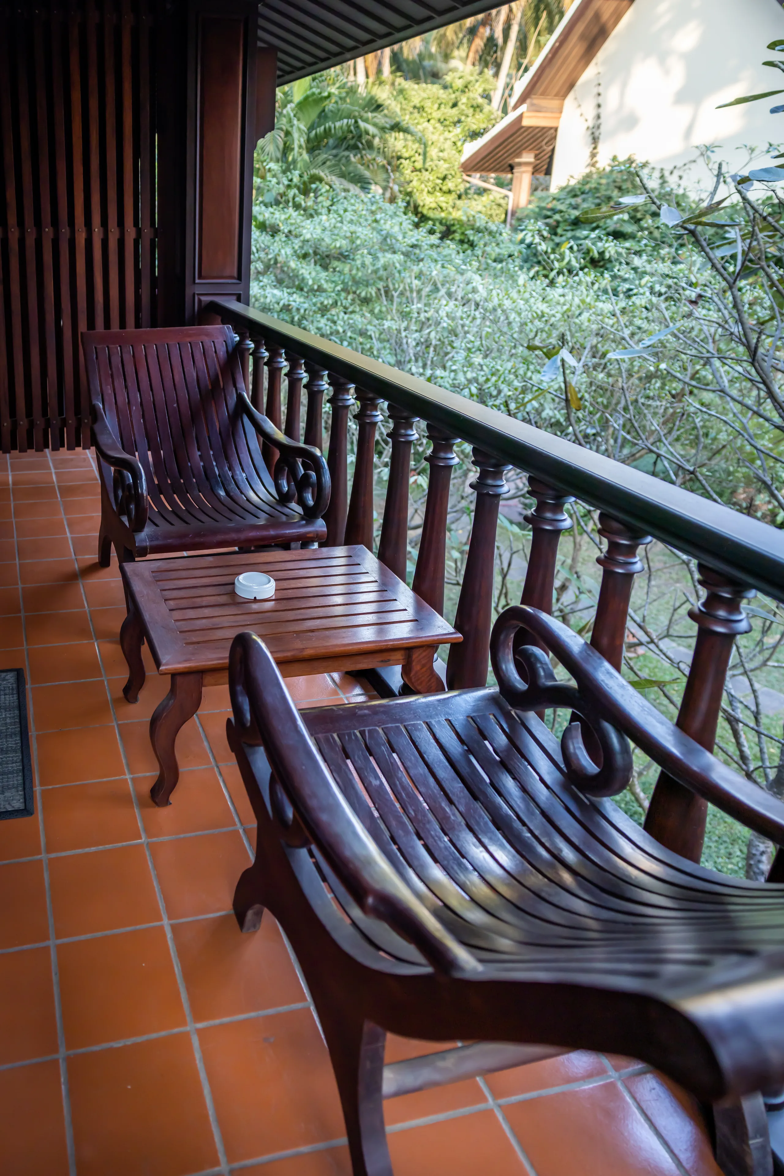 Teak chairs and a low table on a private balcony overlooking the garden