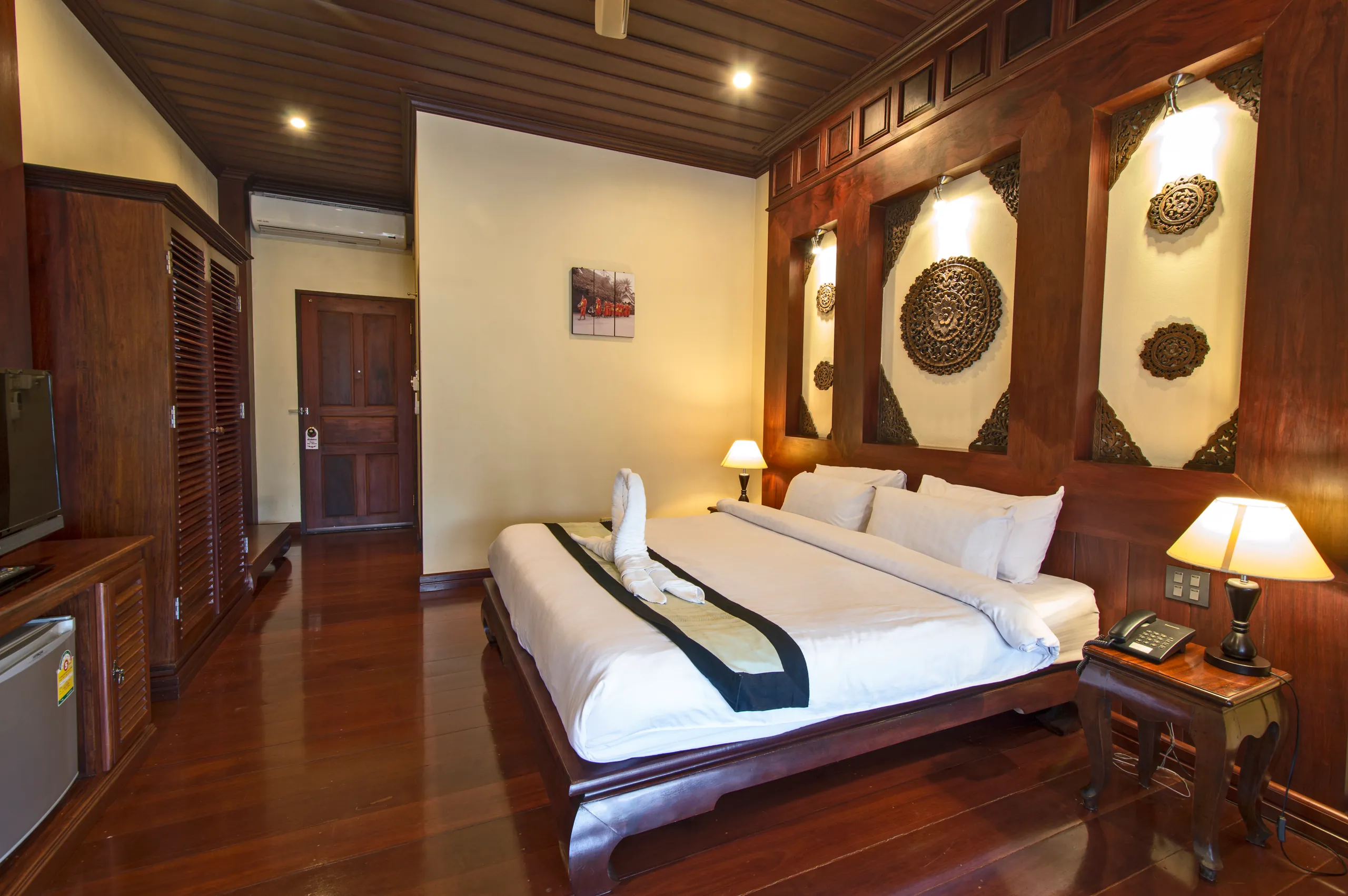 A Deluxe room with a king bed, carved wall medallions and polished teak floor