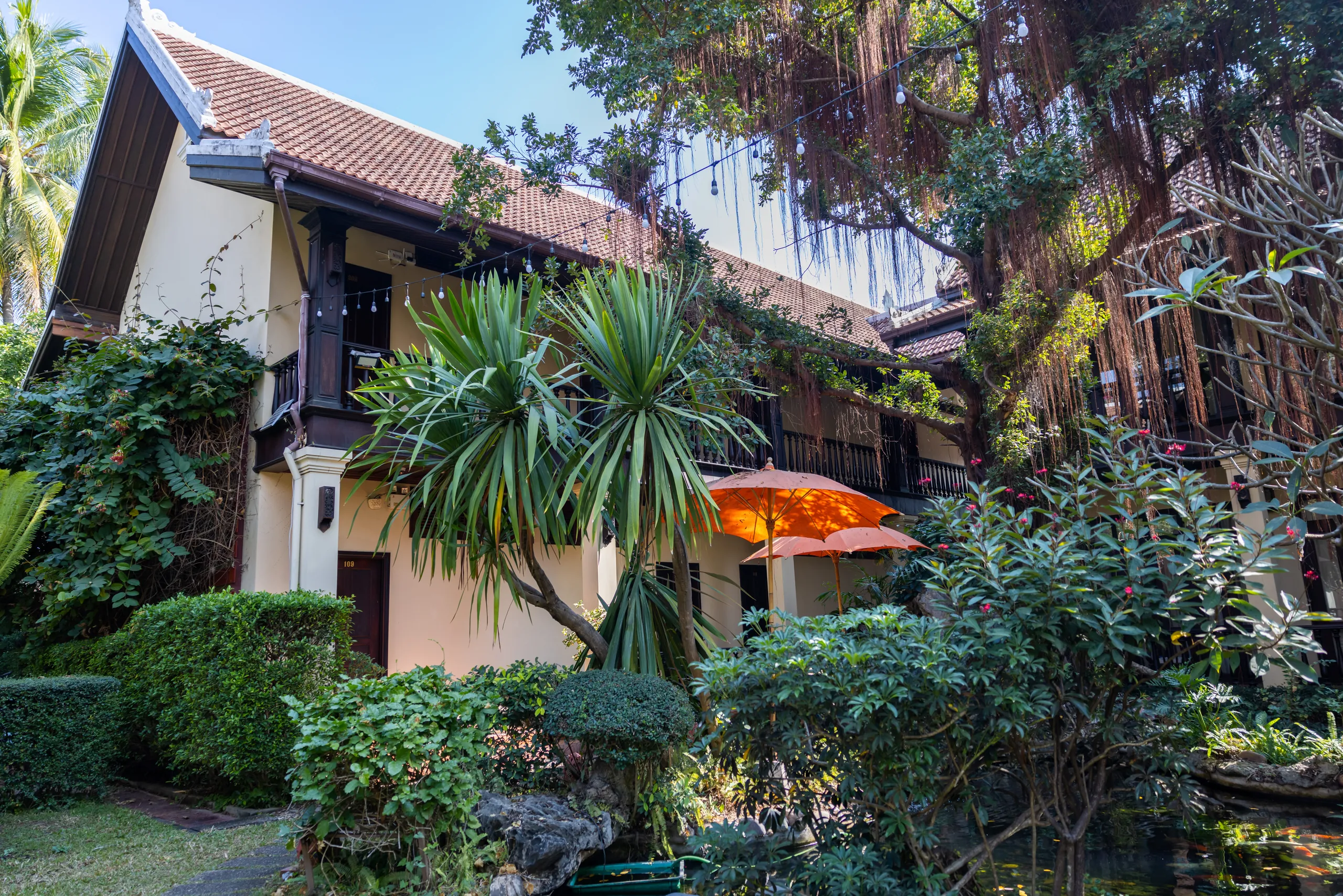 The cream and teak façade of Sada Hotel behind palms and flowering shrubs