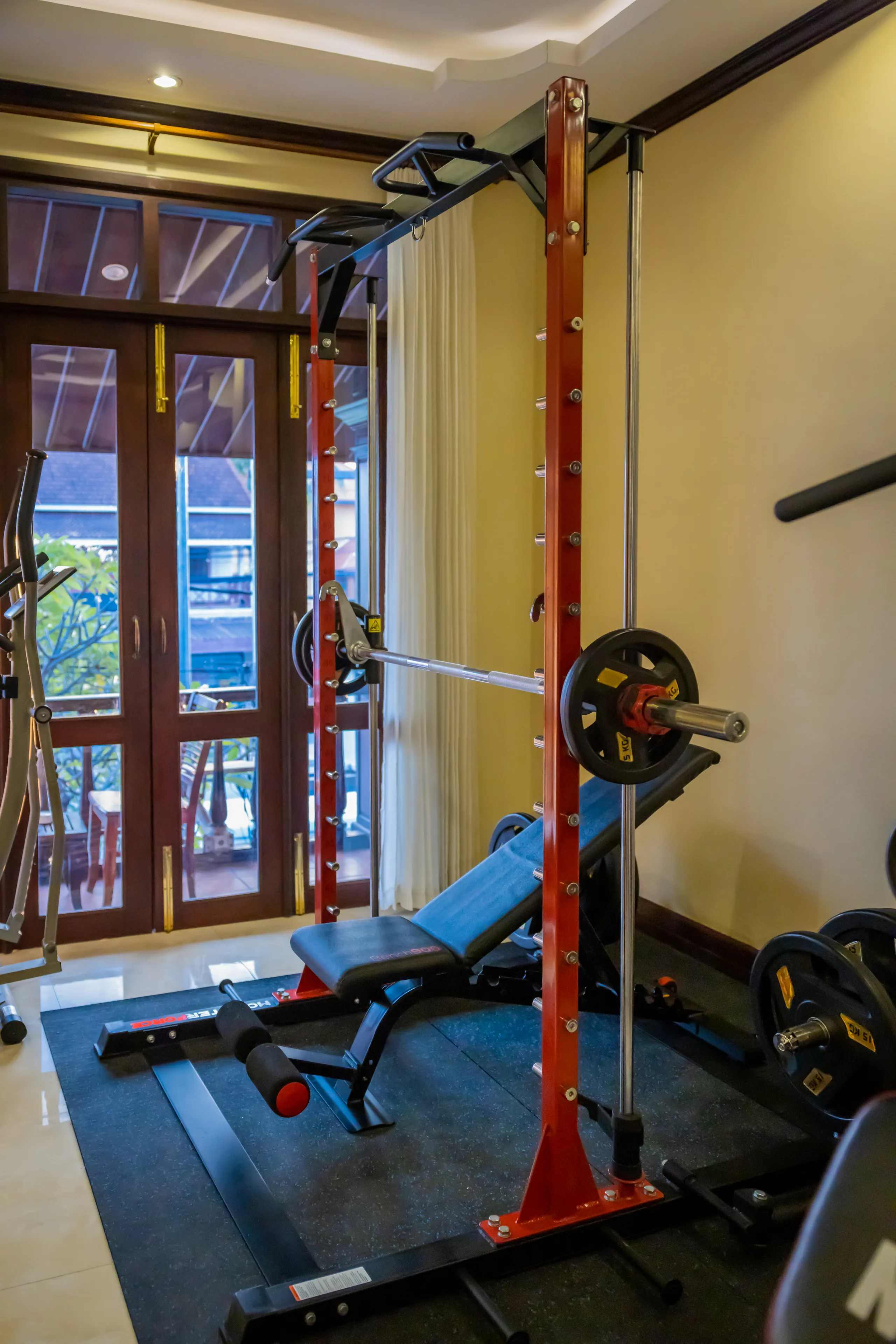The hotel gym with weights rack and equipment beside tall windows