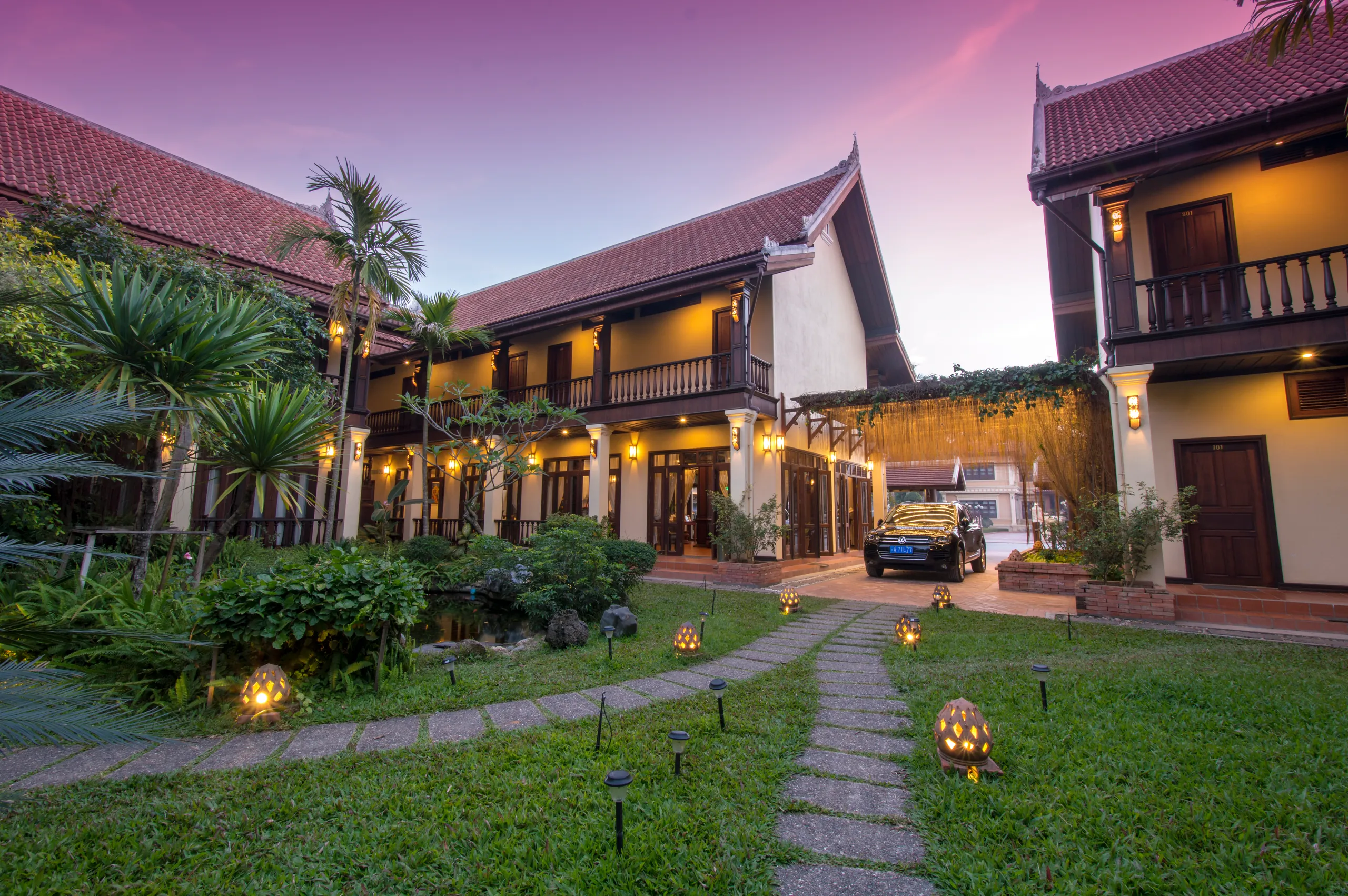 The garden courtyard at dusk under a pink sky, lantern-lit path leading to the main building