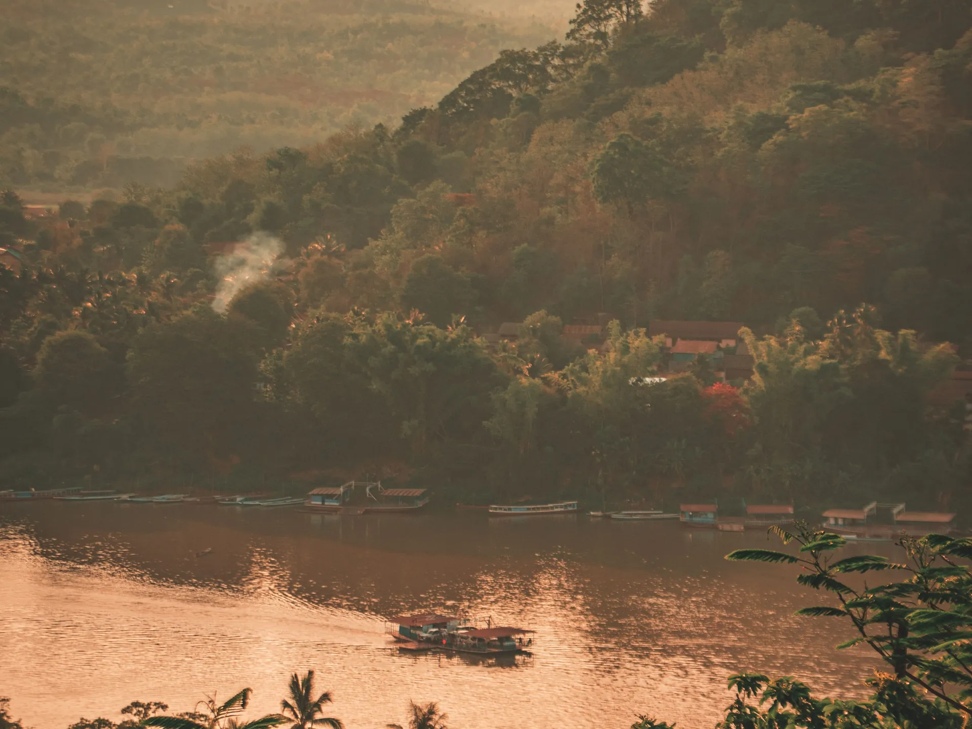 A longboat on the Mekong at dusk, the water gold beneath forested hills