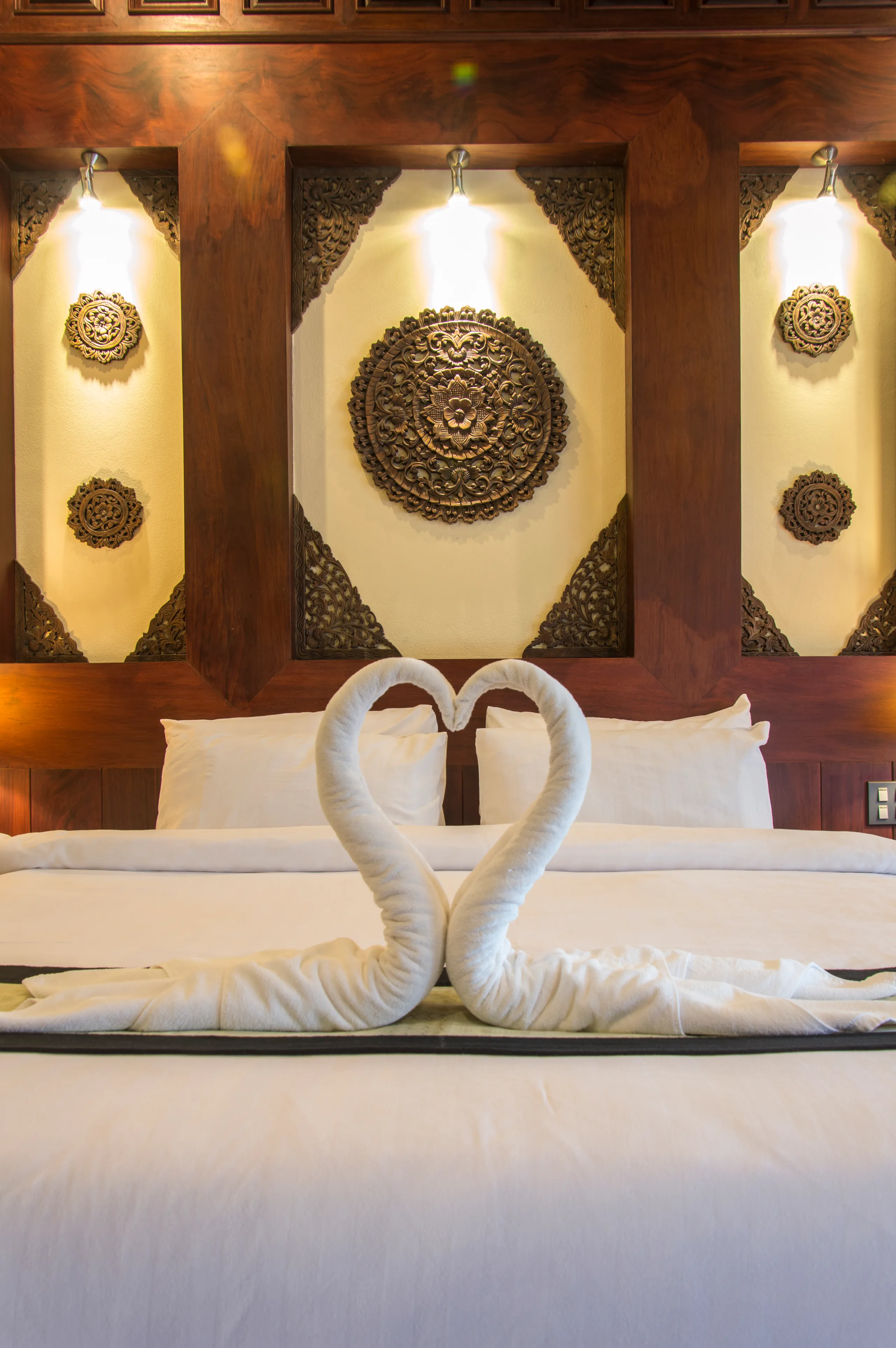 Two towels folded into swans, arranged as a heart on a made bed